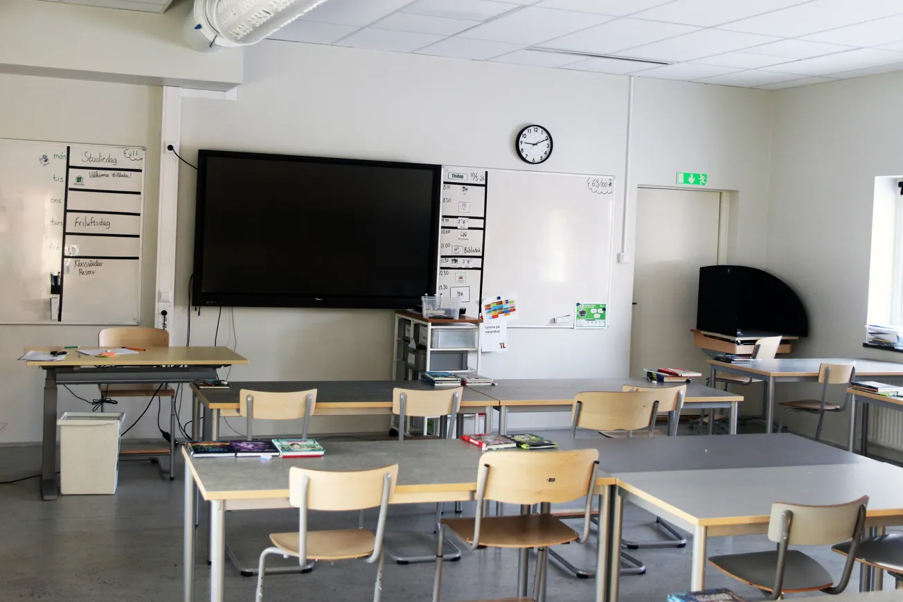 Ett klassrum med skrivbord och stolar och en platt-tv.