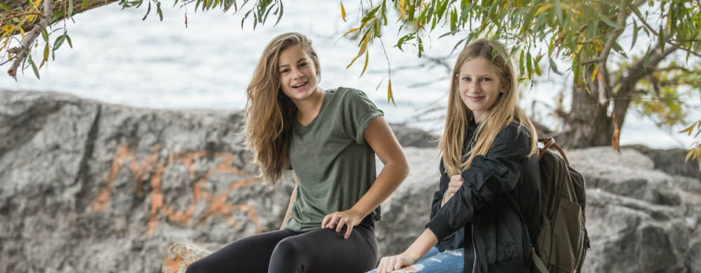 Två unga kvinnor sitter på en klippa nära havet.