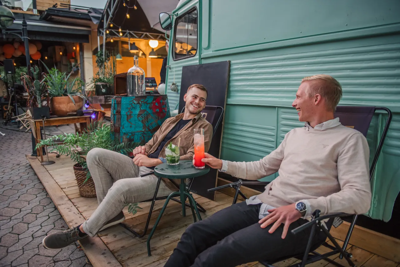 Två män som sitter bredvid varandra med varsin drink på en uteservering.