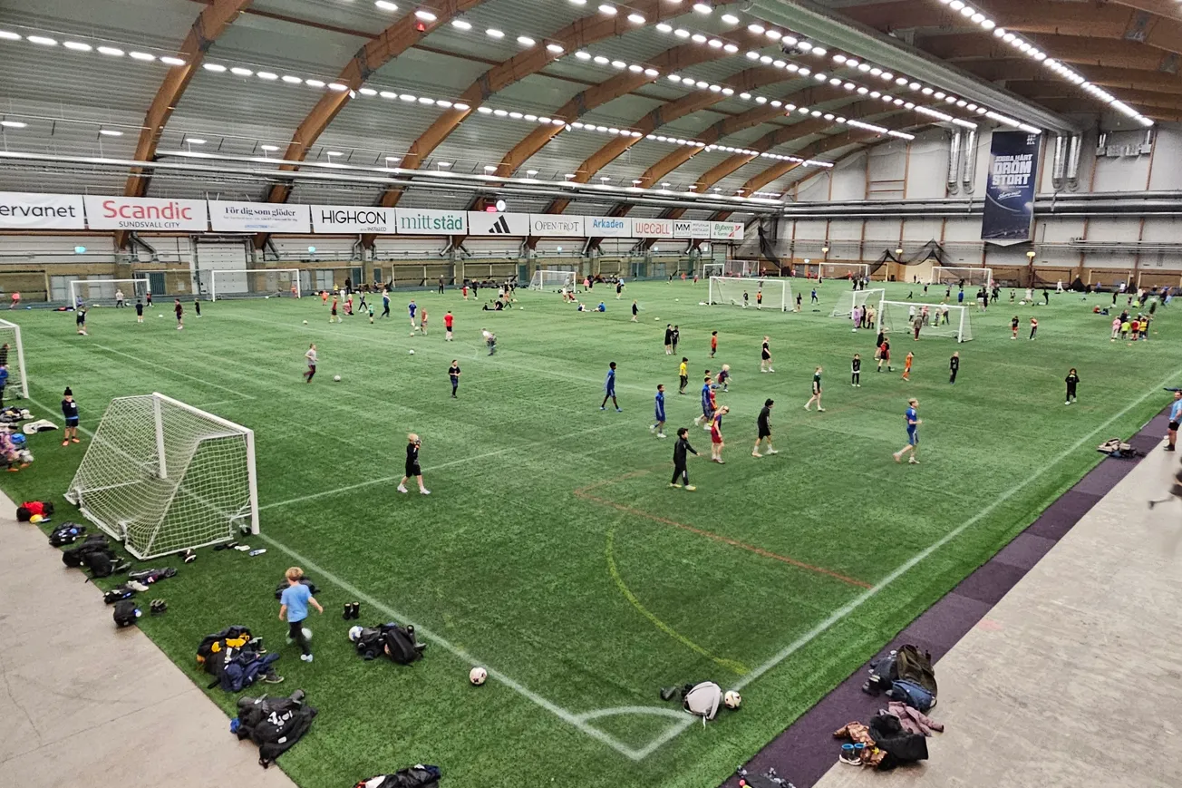 Många personer spelar fotboll på en konstgräsplan inomhus.