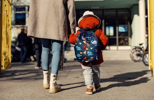 En kvinna och ett barn går på en trottoar med ryggarna mot oss.