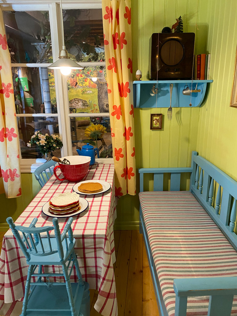 Köksbord med vit och rödrandig duk och blå soffa.