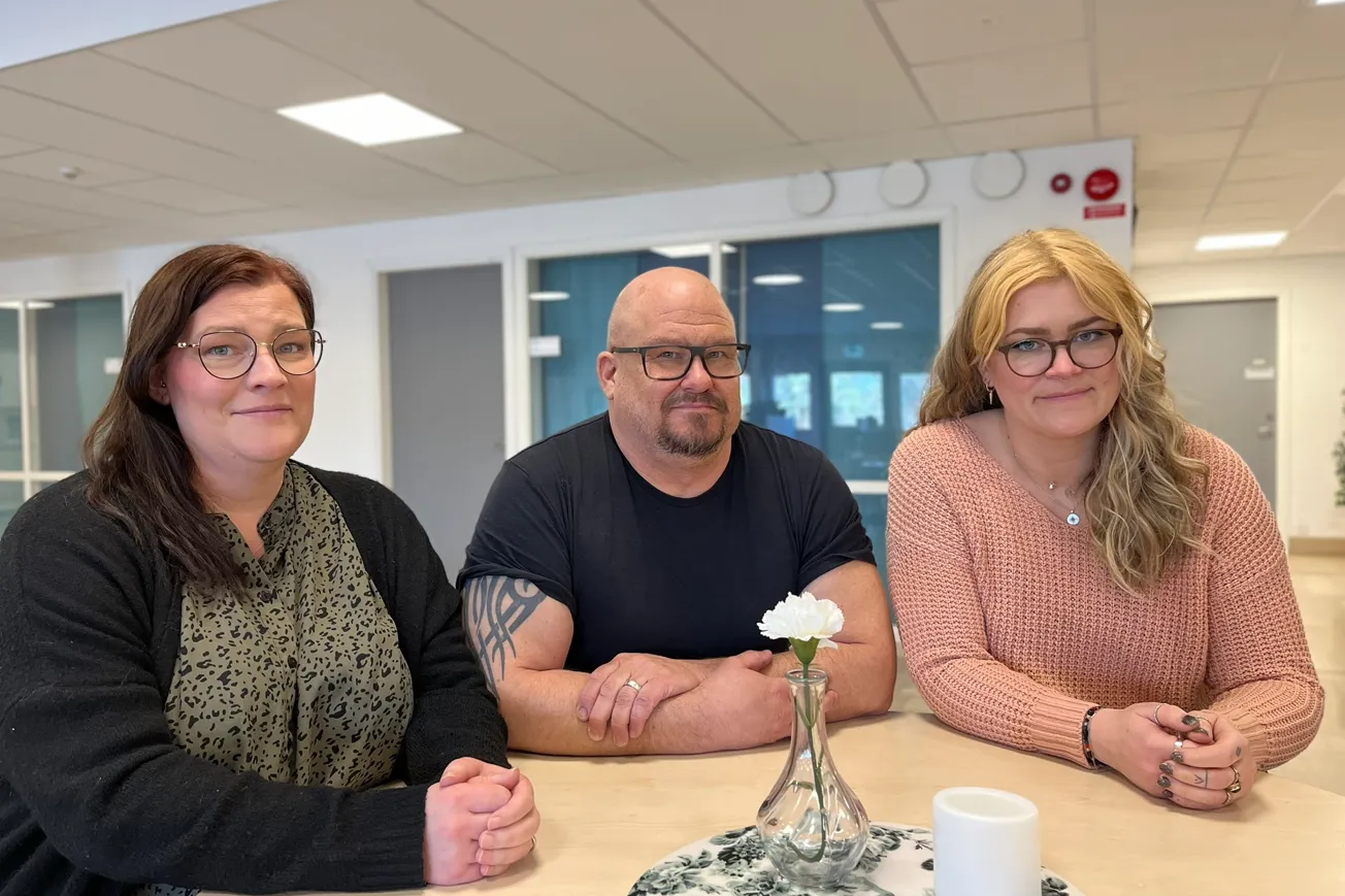 Tre personer som läser fristående kurser vid Vuxenutbildning sitter vid ett bord med en vas med blommor.