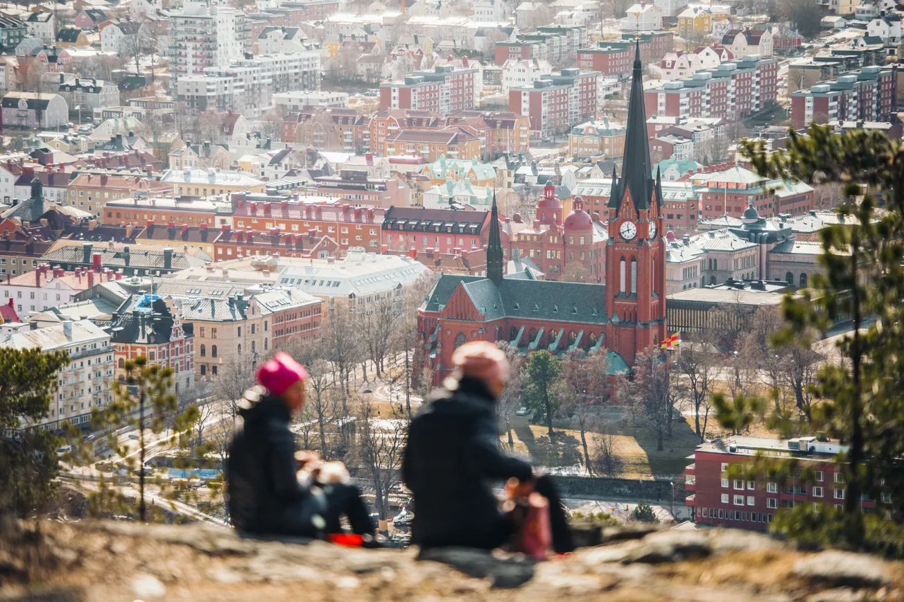 Två personer sitter på en kulle med utsikt över en stad.