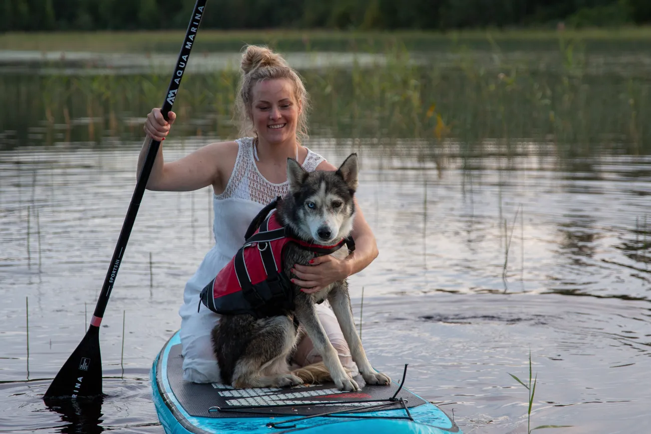 En kvinna som paddlar på en sup på sjön. På suppen är det även en hund hon kramar om.