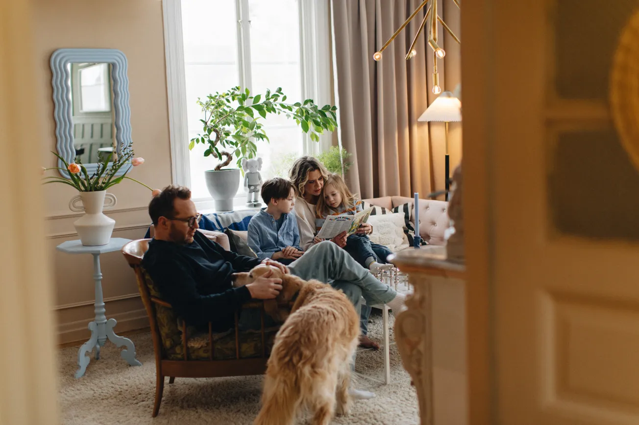 Familj om fyra personer och en hund umgås tillsammans i vardagsrum.