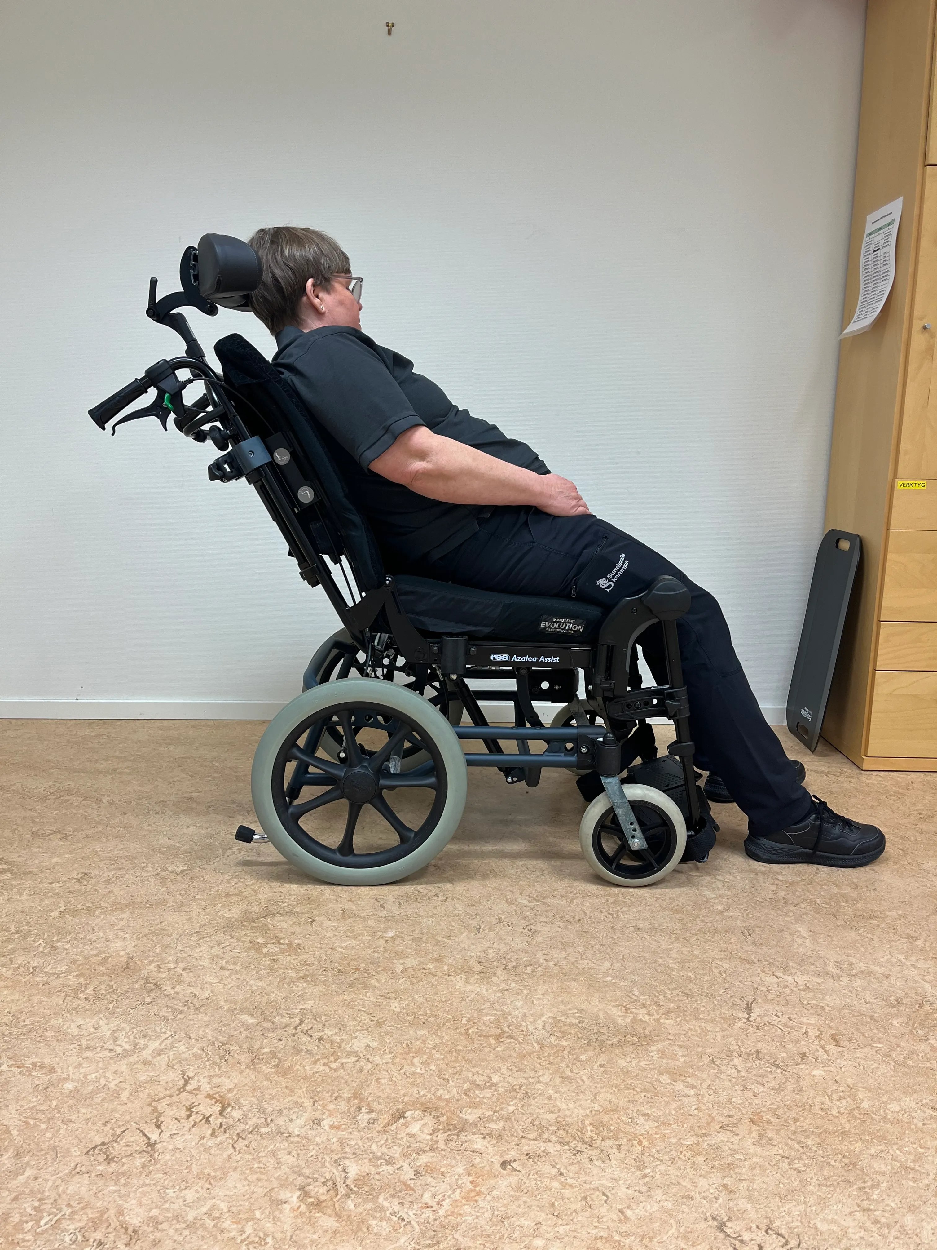 En person sitter lutad bakåt i en rullstol.