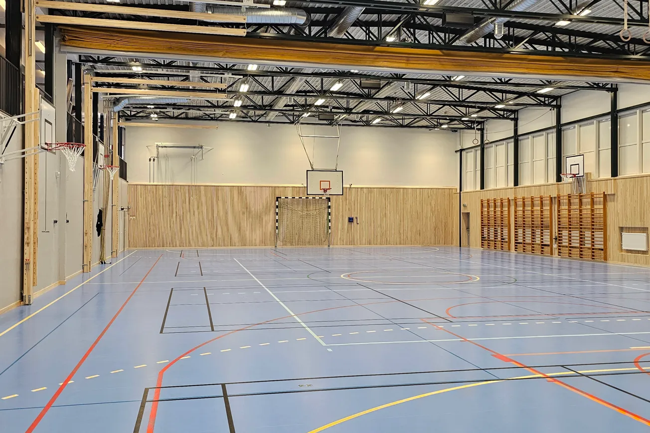 Idrottshall med linjer på golvet och utrustning för gymnastik på väggarna.