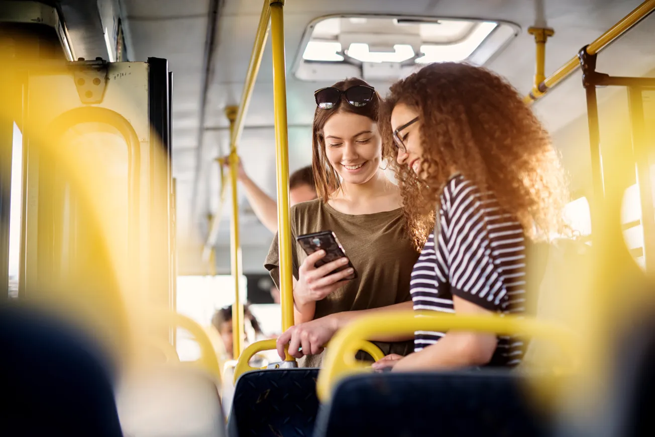 Två kvinnor på en buss som tittar på en mobiltelefon.