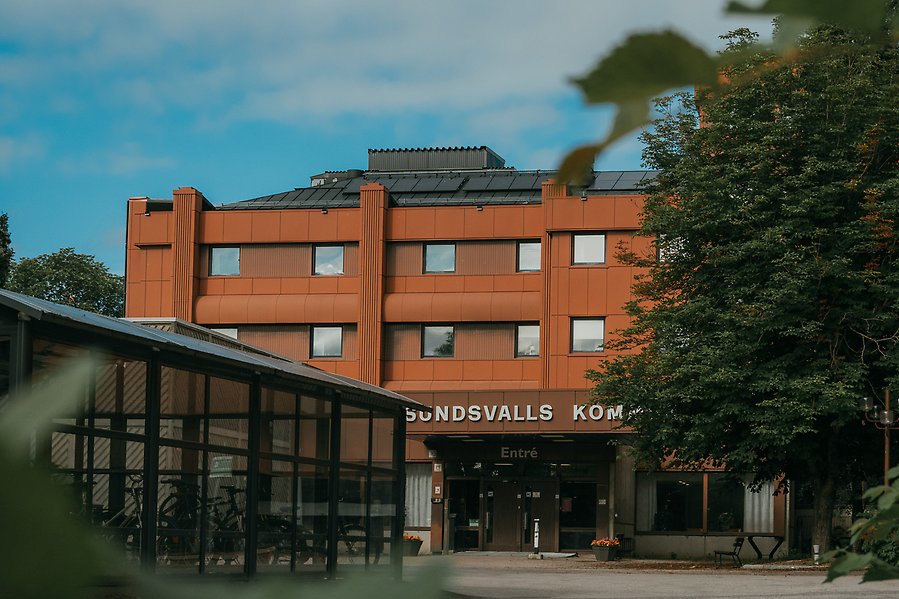 Sundsvalls kommunhus entré i bakgrunden av ett svart cykelgarage och lummigt grönt träd. 