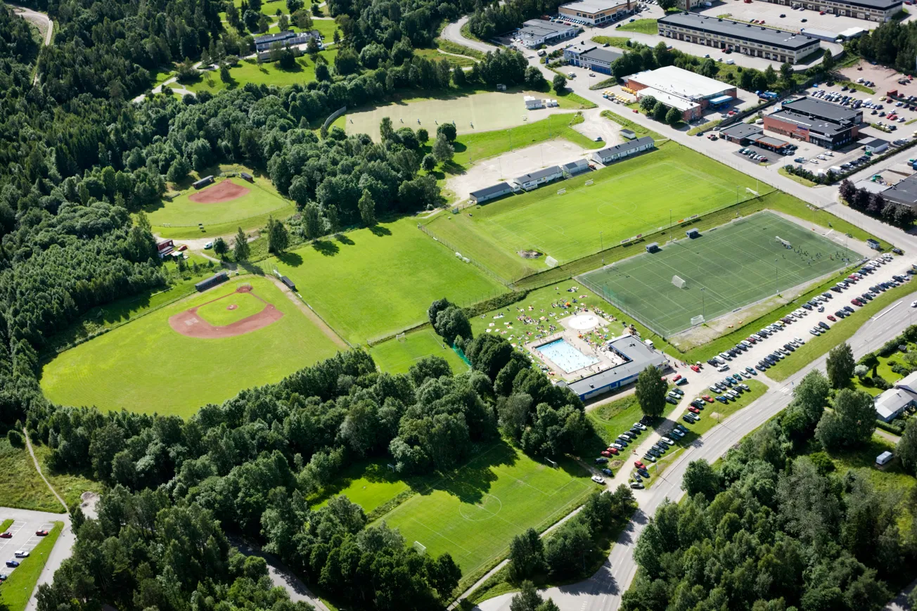 Flygfoto över idrottsanläggning med bollplaner och ett utomhusbad.