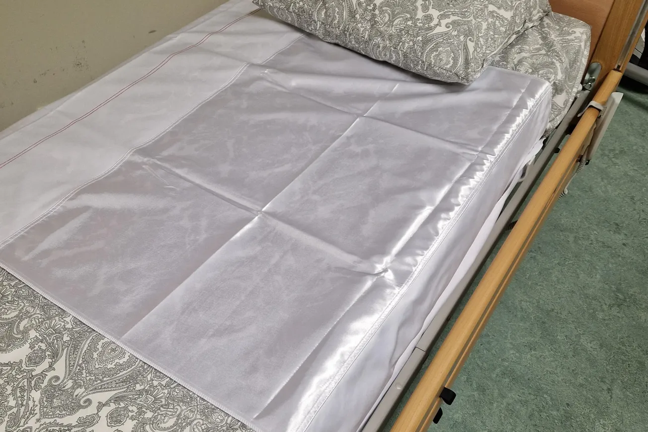 En säng med ett vitt glidlakan och en kudde på. Glidlakanet är felplacerat.