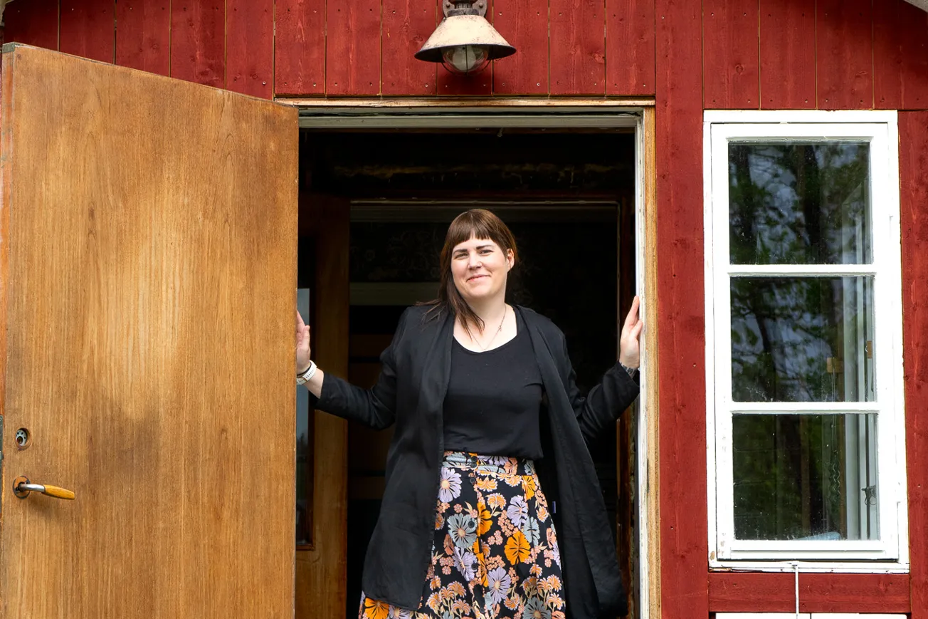 En kvinna som står i dörröppningen till ett rött hus.