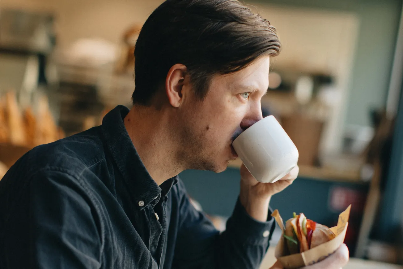 Man dricker kaffe ur mugg och håller i en smörgås.