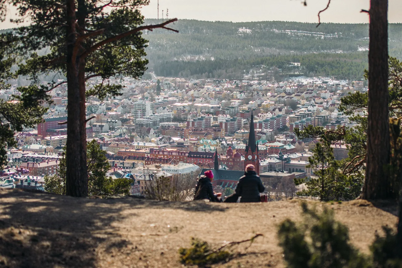 Två personer sitter på en kulle med utsikt över en stad.