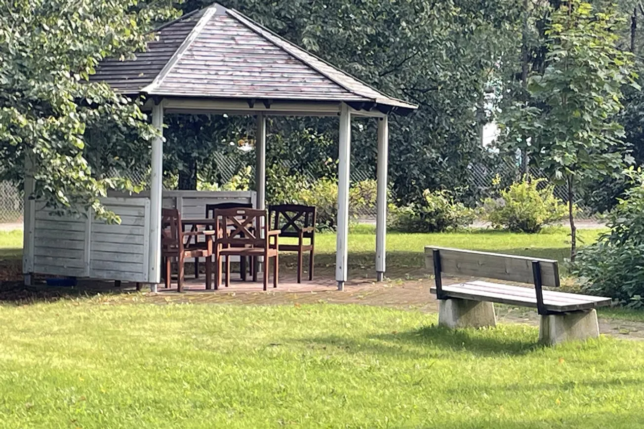 En träbänk som sitter under ett lusthus av trä.