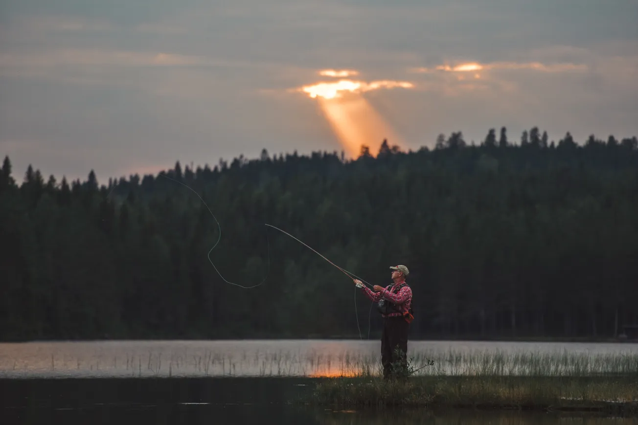 En man som flugfiskar i vattenbrynet i solnedgången.