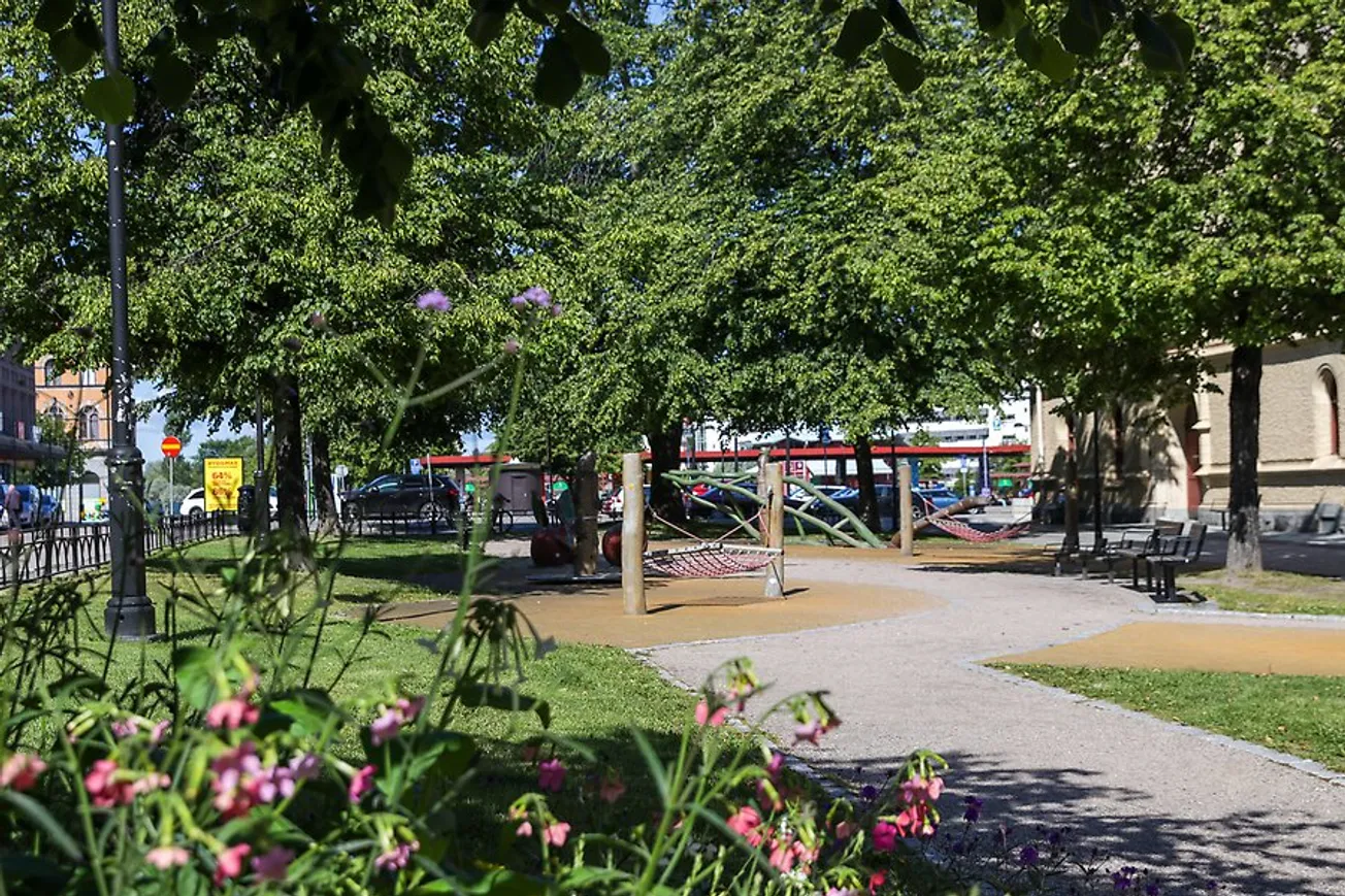 Magasinsparken sommartid. Blommor i förgrunden och lekutrustning och träd.