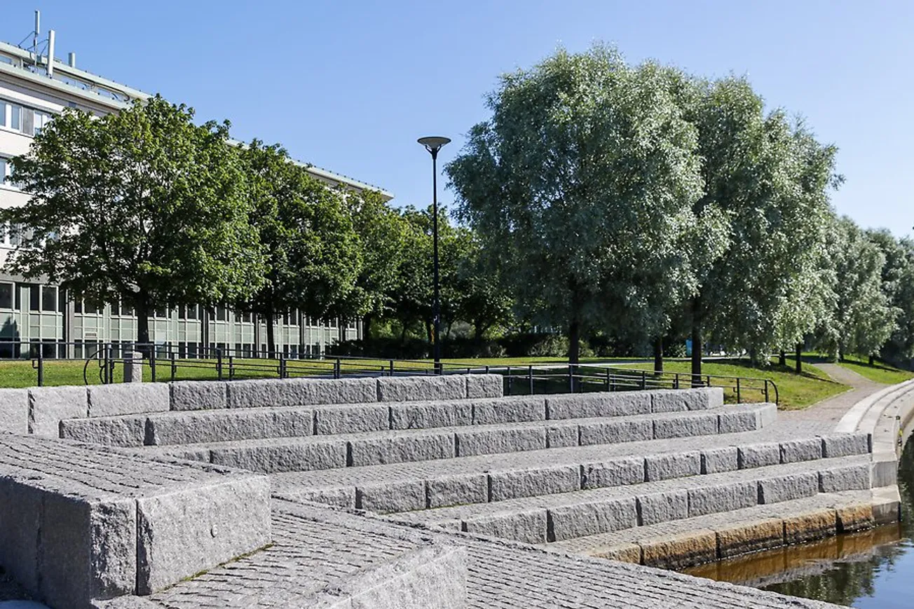 En stentrappa vid Selångersån vid Norrmalmsparken sommartid. Träd syns i bakgrunden.