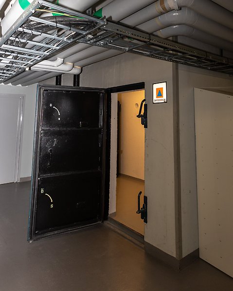 En robust dörr står öppen och en skylt intill för skyddsrum.