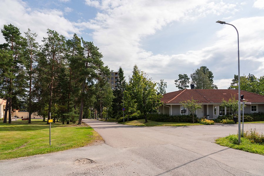 Illustration av byggnad som syns bakom träd från ett villaområde.