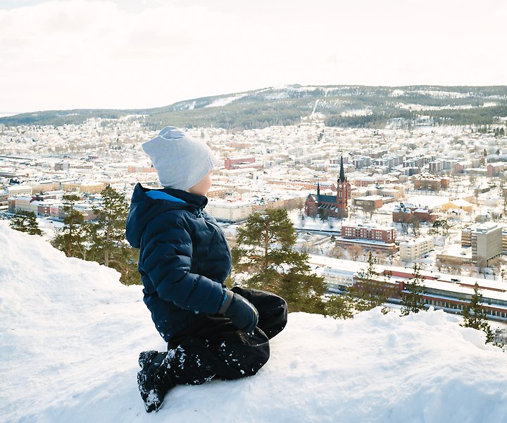 En person som sitter på toppen av en snötäckt kulle med en stad i bakgrunden.