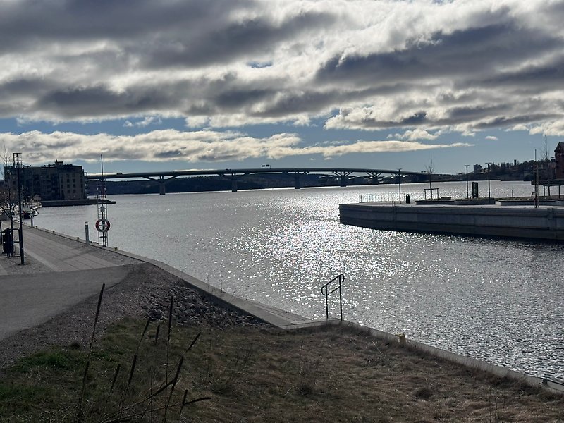 Vy över vattenområde och kajpromenad med trappor ner till vattnet. I bakgrunden syns Sundsvallsbron.