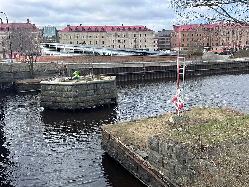 Gamla stenfundament från en tidigare bro över Selångersån syns i vattnet framför kajområdet vid Kulturmagasinet. I bakgrunden syns kaj, byggnader och pågående arbete längs vattnet.
