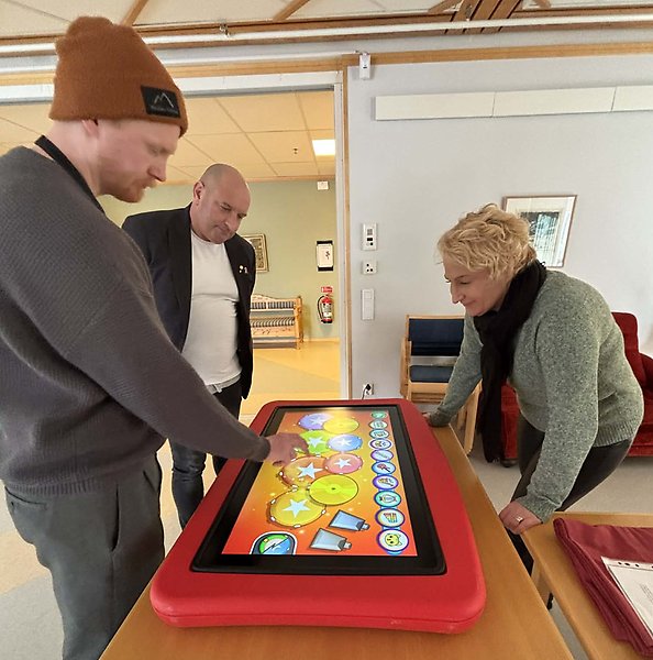Tre personer som står runt ett bord med en stor surfplatta.