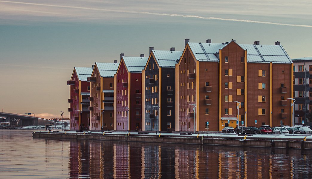 Fem högre trähus intill vatten med vattenspegling av husen. 